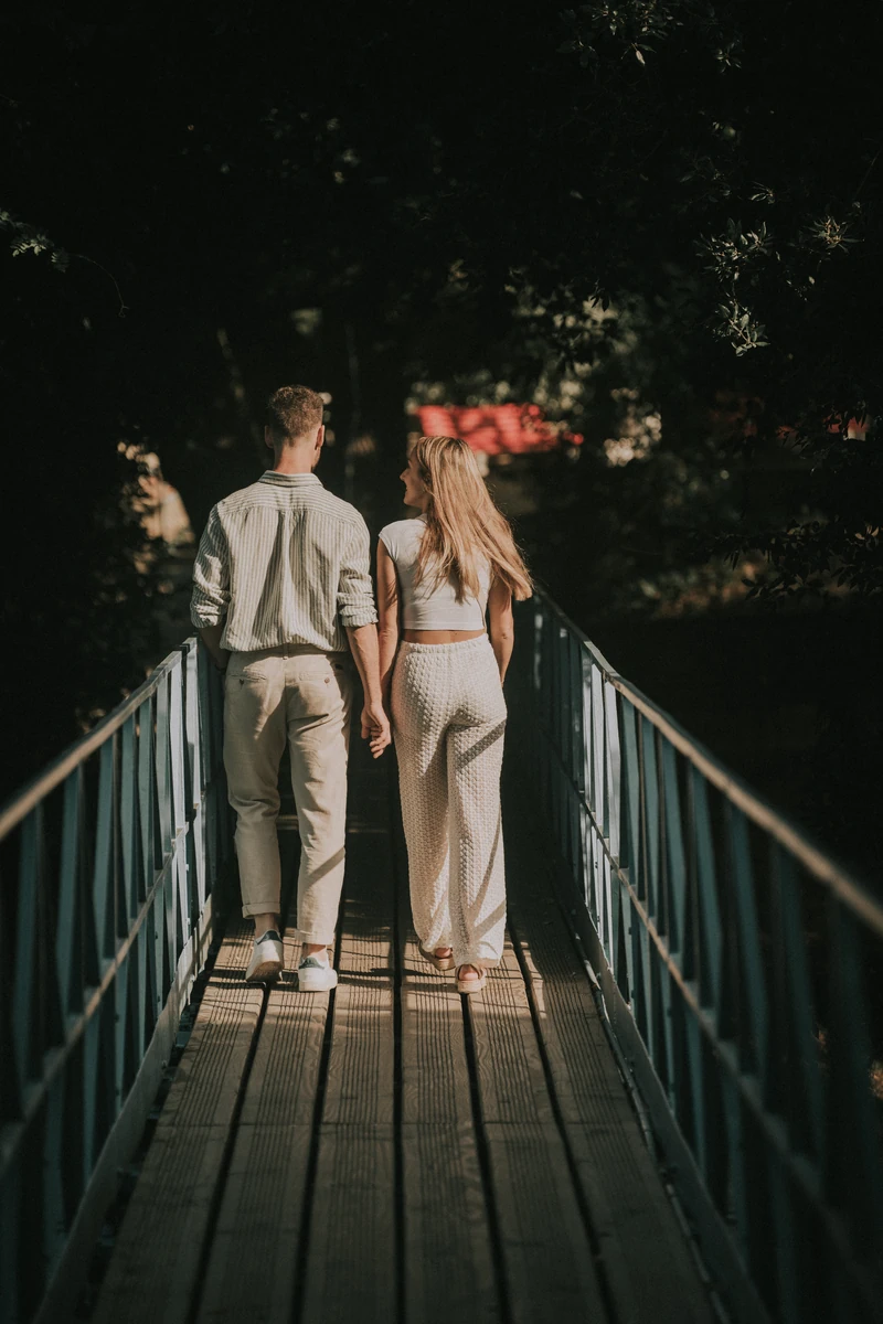 Photo de couple à Arcachon – Marine et Théo main dans la main sur une passerelle en bois dans un parc arboré.
