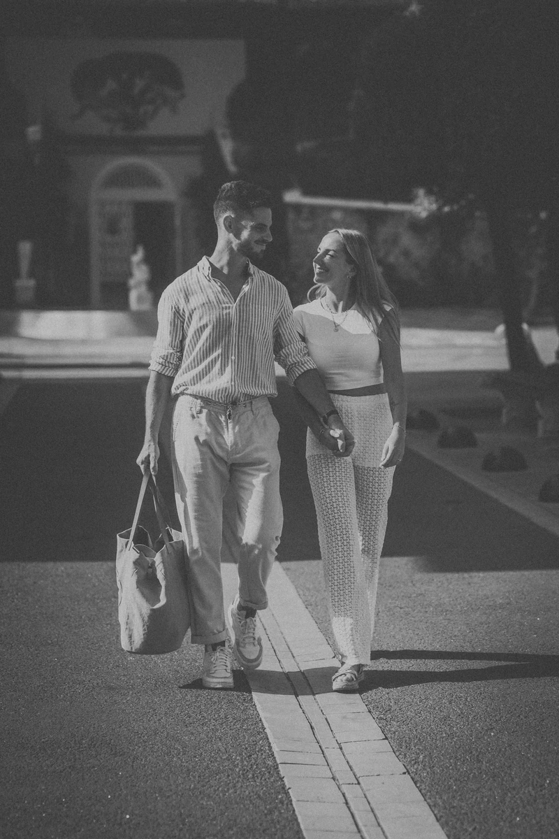 Séance photo couple à Arcachon, Marine et Théo marchent main dans la main dans une ruelle ensoleillée.