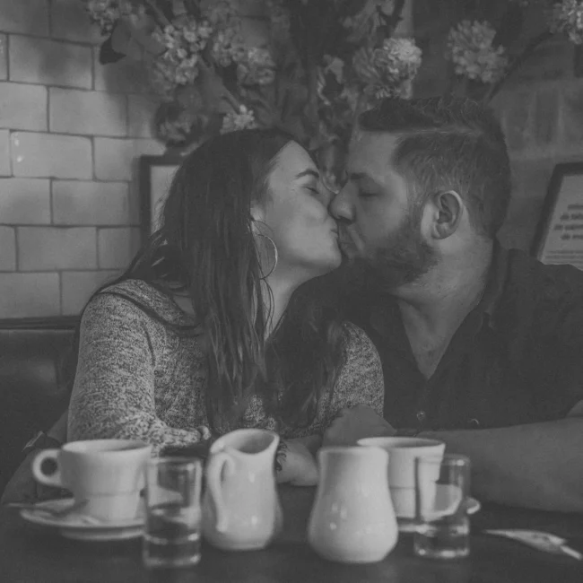Couple s’embrassant dans un café cosy à Arcachon, ambiance intime et lifestyle en noir et blanc