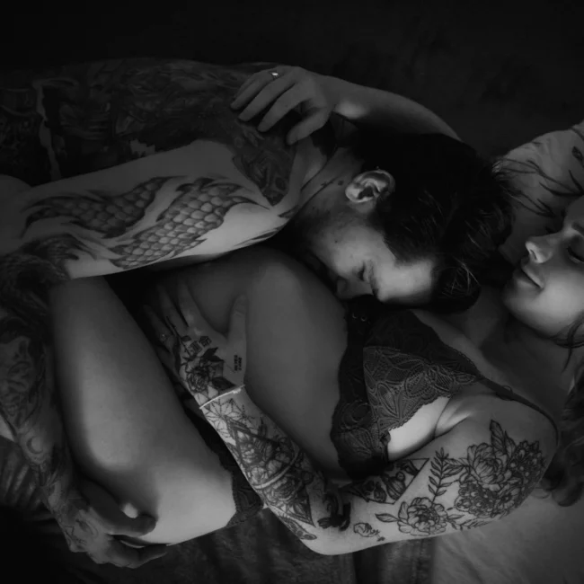 Photographe grossesse à domicile – couple tatoué en noir et blanc dans une étreinte intime