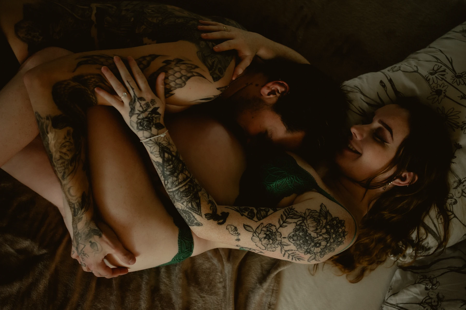 Séance grossesse lifestyle, couple tatoué enlacé sur lit à domicile – moment intime et complice