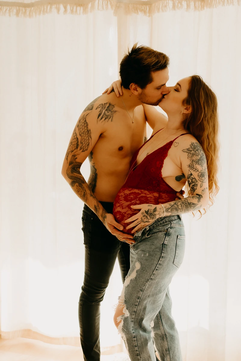 Photo grossesse lifestyle – couple s’embrassant tendrement, main sur le ventre rond