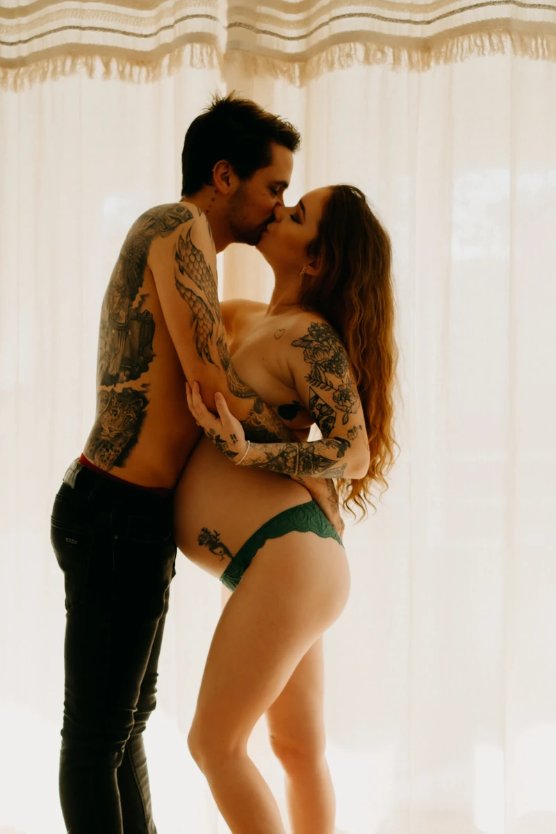 Séance grossesse lifestyle à domicile – couple s’embrassant tendrement en lumière naturelle