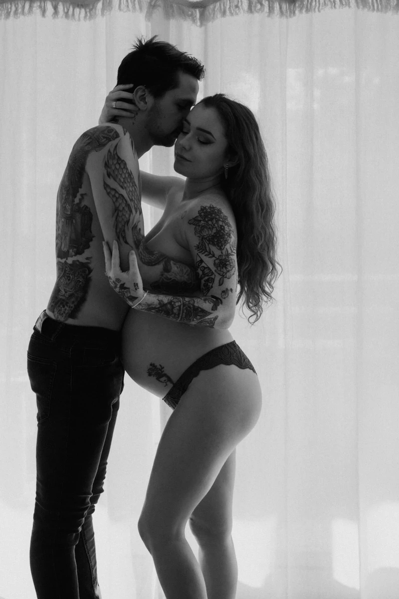 Photographe grossesse : photo artistique en noir et blanc d’un couple enlacé pendant une séance lifestyle à domicile