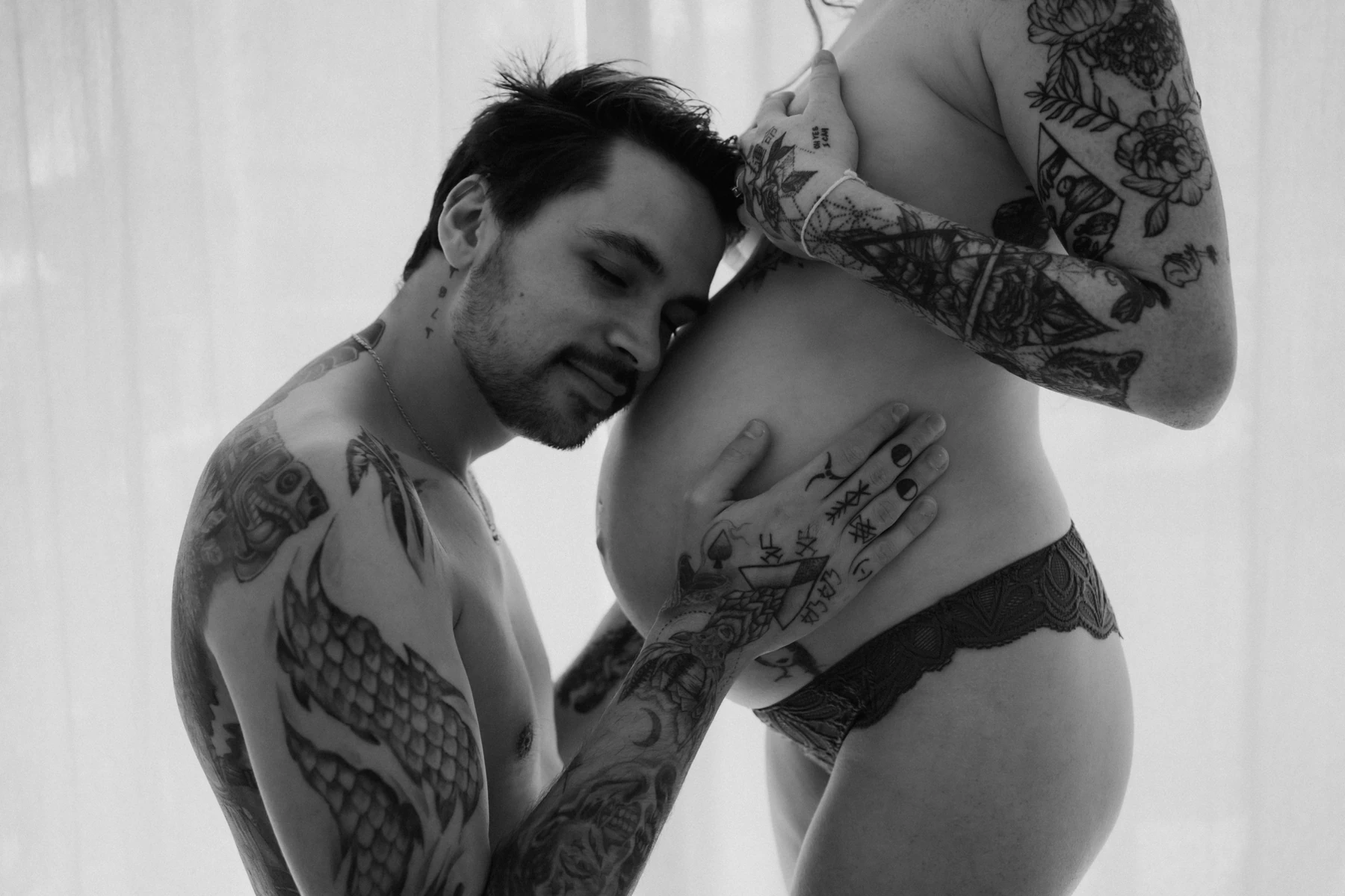 Futur papa tatoué embrassant tendrement le ventre arrondi de sa compagne enceinte