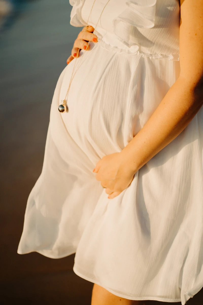 vent léger sur une robe blanche de future maman au bord de l’eau, séance grossesse douce et lumineuse à Pyla-sur-Mer