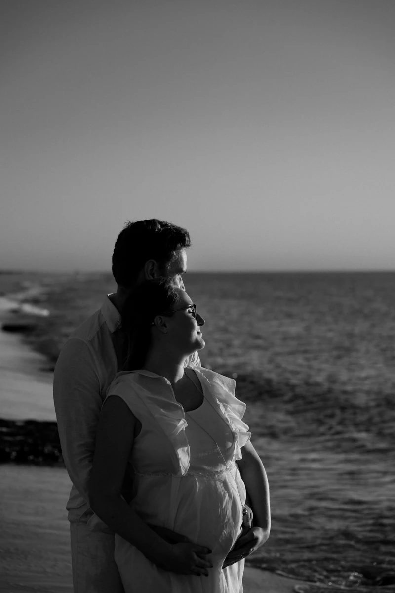 Futurs parents enlacés en noir et blanc face à l’océan au Pyla-sur-Mer