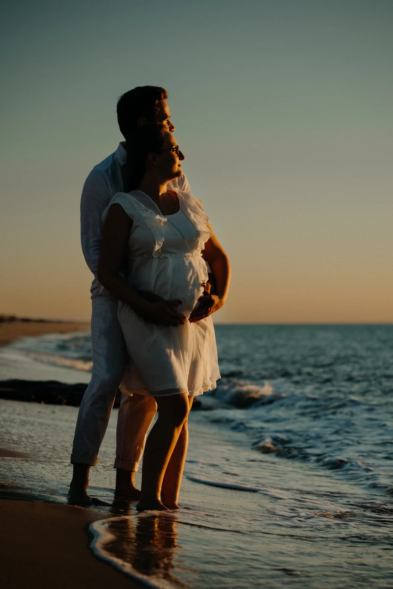 Couple de futurs parents enlacés au bord de l’océan au coucher du soleil