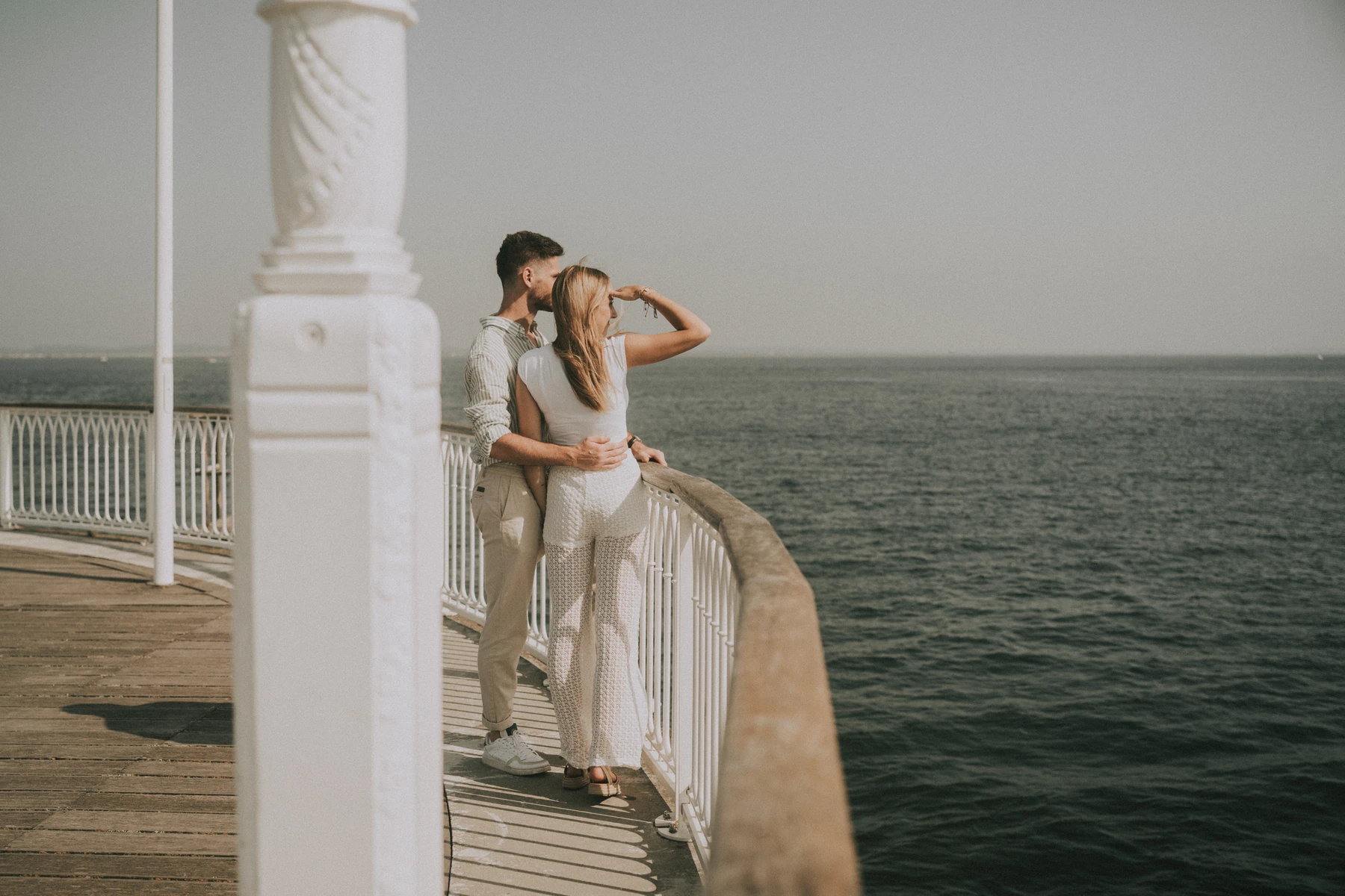 Photo de couple enlacé au bout de la jetée d’Arcachon, vue sur le Bassin sous la lumière du matin.