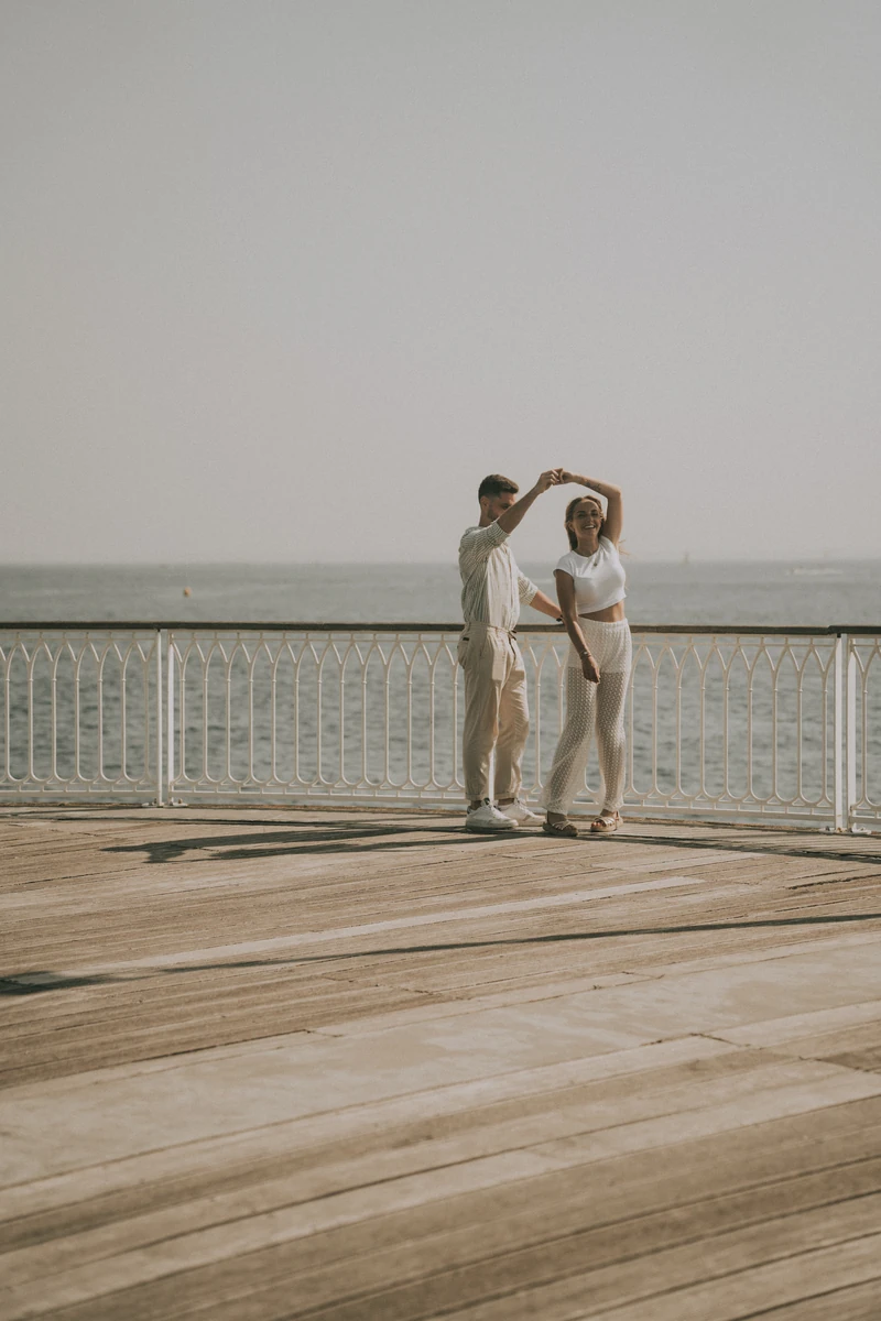 Photo de couple dansant sur la jetée en bois au bord de la plage à Arcachon, lumière douce du matin.