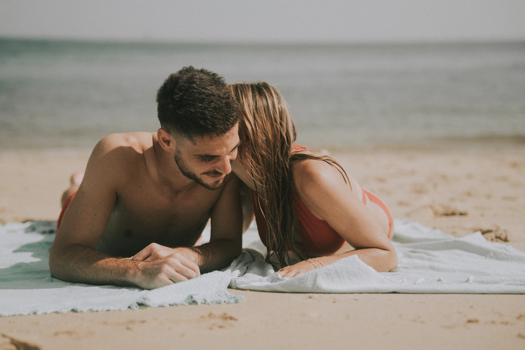 Séance couple à la plage avec Marine et Théo allongés sur le sable, regard complice en bord de mer à Arcachon.