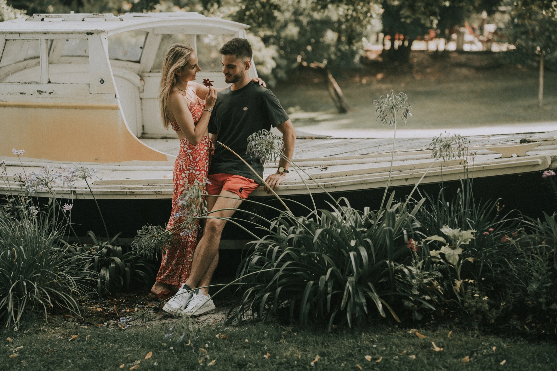 Marine et Théo échangent un regard complice près d’un bateau dans un parc verdoyant lors d’une séance photo lifestyle à Arcachon.