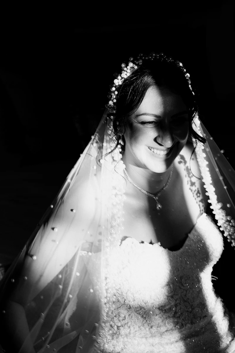 Portrait lumineux d'une mariée souriante sous son voile perlé, photo de mariage en noir et blanc
