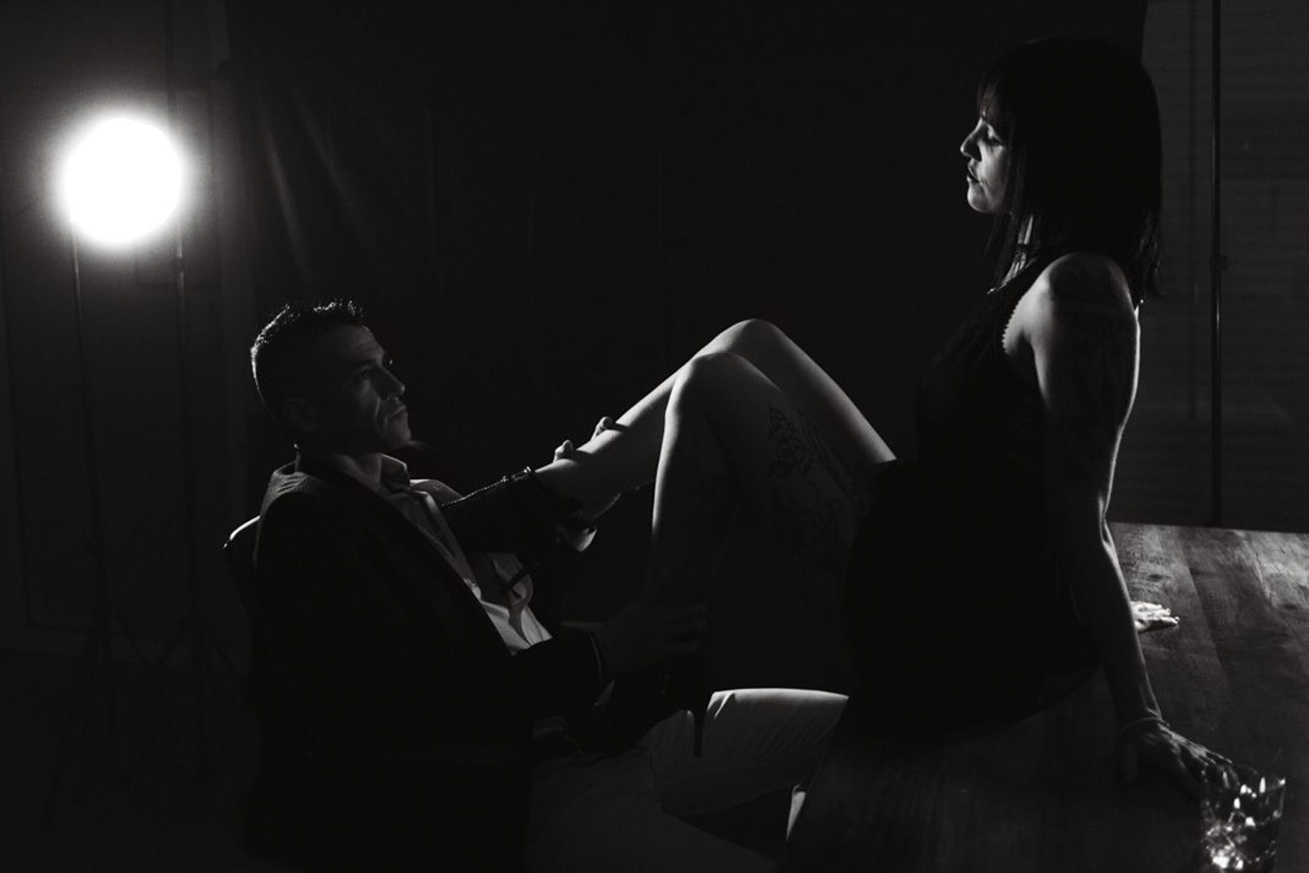 Séance boudoir noir et blanc d’un couple avec lumière dramatique, poses cinématographiques et jeu de regards.